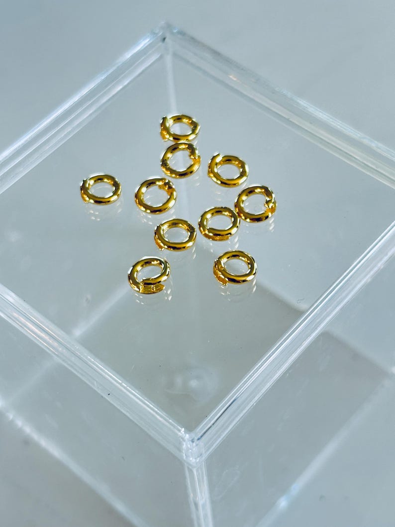 Pu&ograve; includere: Una scatola di plastica trasparente piena di 12 anelli di salto dorati. Gli anelli di salto sono piccoli e rotondi, e sono disposti a forma di stella.
