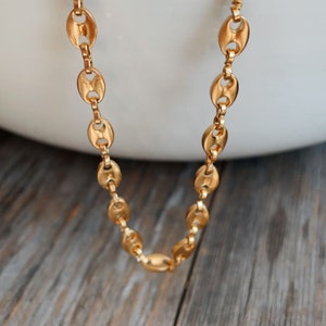 May include: A gold chain necklace with a classic oval link design. The chain is laying on a wooden surface.