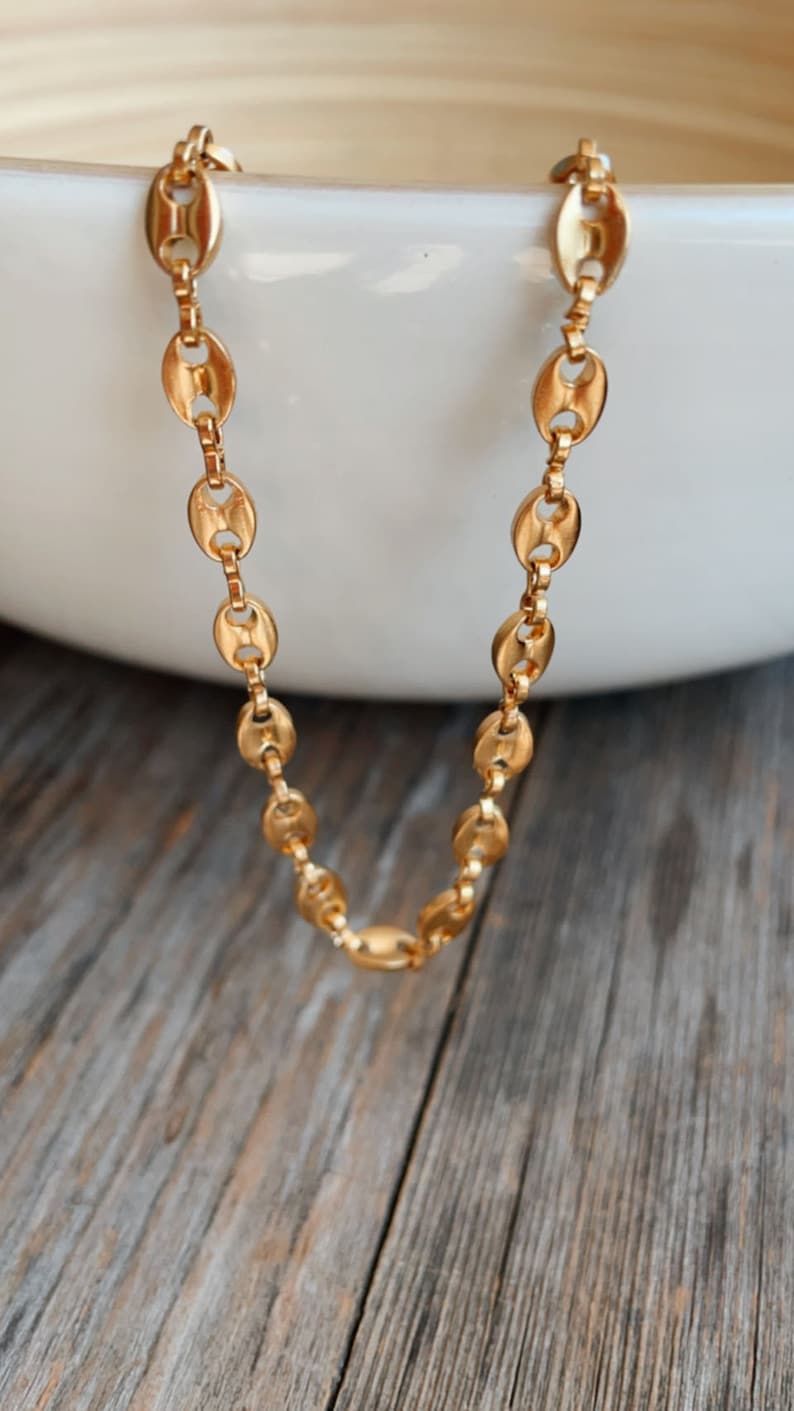 May include: A gold chain necklace with a classic oval link design. The chain is laying on a wooden surface.