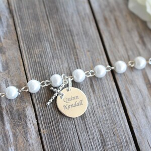 May include: A silver bracelet with white pearl beads and a silver charm with the name "Quinn Kendall" engraved on it.