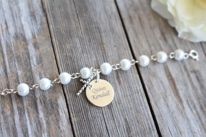 May include: A silver bracelet with white pearl beads and a silver charm with the name "Quinn Kendall" engraved on it.