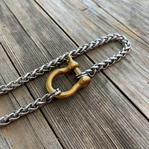 Pu&ograve; includere: Una catena d'argento con una chiusura a forma di U dorata. La catena e la chiusura sono su una superficie di legno.