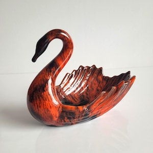 May include: A swan-shaped bowl featuring a glossy finish with a marbled pattern of deep black and vibrant orange. The sculpture has a curved neck and a body with textured, wing-like edges that form a shallow basin for holding small items.