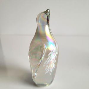 May include: Iridescent glass art piece in a teardrop shape. The glass has a pearlescent finish with rainbow hues and white accents. The top of the piece curves gracefully. A decorative item for display.