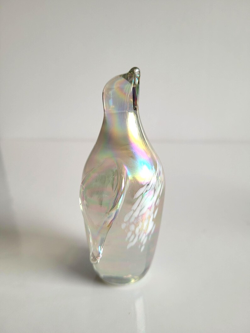 May include: Iridescent glass art piece in a teardrop shape. The glass has a pearlescent finish with rainbow hues and white accents. The top of the piece curves gracefully. A decorative item for display.