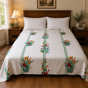 May include: A white bed sheet featuring vertical green stripes and a repeating floral pattern of orange, red, and blue lilies with green leaves. The fabric is draped over a bed with two white pillows, positioned between two wooden nightstands.