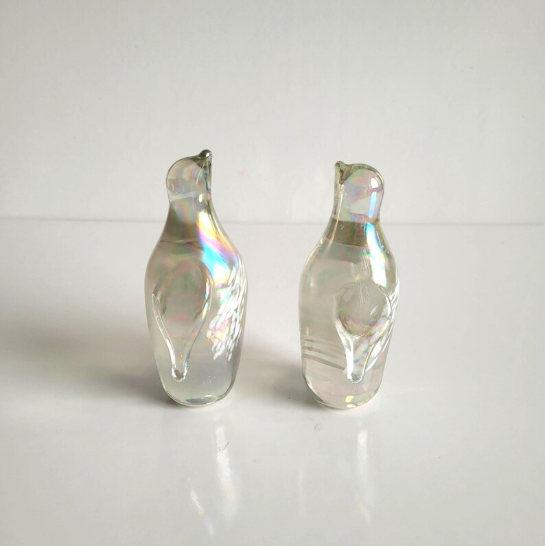 May include: Two iridescent glass decorative bottles with a pearlescent finish. The bottles have a curved shape with a small opening at the top and a teardrop-shaped design on the front. The glass reflects a rainbow of colors.