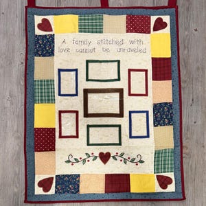 May include: A patchwork wall hanging with a central panel for photos and embroidered text. The text reads "A family stitched with love cannot be unravelled." The border features hearts and various fabric patterns.