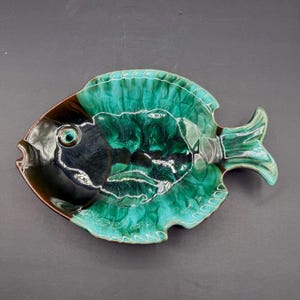 May include: A ceramic dish shaped like a fish with a glossy glaze. The head area is dark brown and black, transitioning into a vibrant emerald green body with darker green and black accents. The surface features a textured, flowing pattern.
