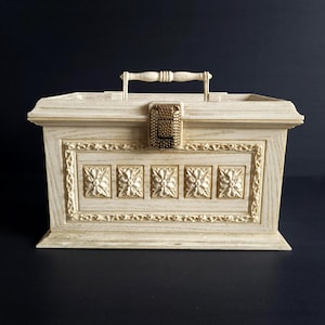 May include: Cream-coloured wooden box with a handle and a decorative front panel. The box features a gold-coloured clasp and five square floral designs. The handle and floral details add to the vintage aesthetic.
