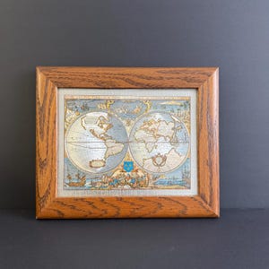 以下が含まれることがあります： 額装されたヴィンテージの世界地図プリント。 地図は、航海要素を備えた詳細でカラフルなイラストで、中程度のオーク材の木材で額装されています。 地図は大陸と海を示し、上部にテキストがあります。