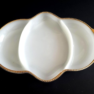Puede incluir: Una fuente blanca de tres secciones con borde festoneado y ribete dorado con cuentas. El plato tiene un acabado brillante y está diseñado para servir aperitivos o snacks. La forma general es oblonga.