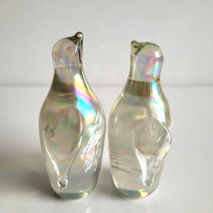 May include: Two clear glass decorative bottles with iridescent rainbow coloring. The bottles have a unique shape with a curved top and a teardrop-shaped design on the side. The bottles are displayed on a white surface.