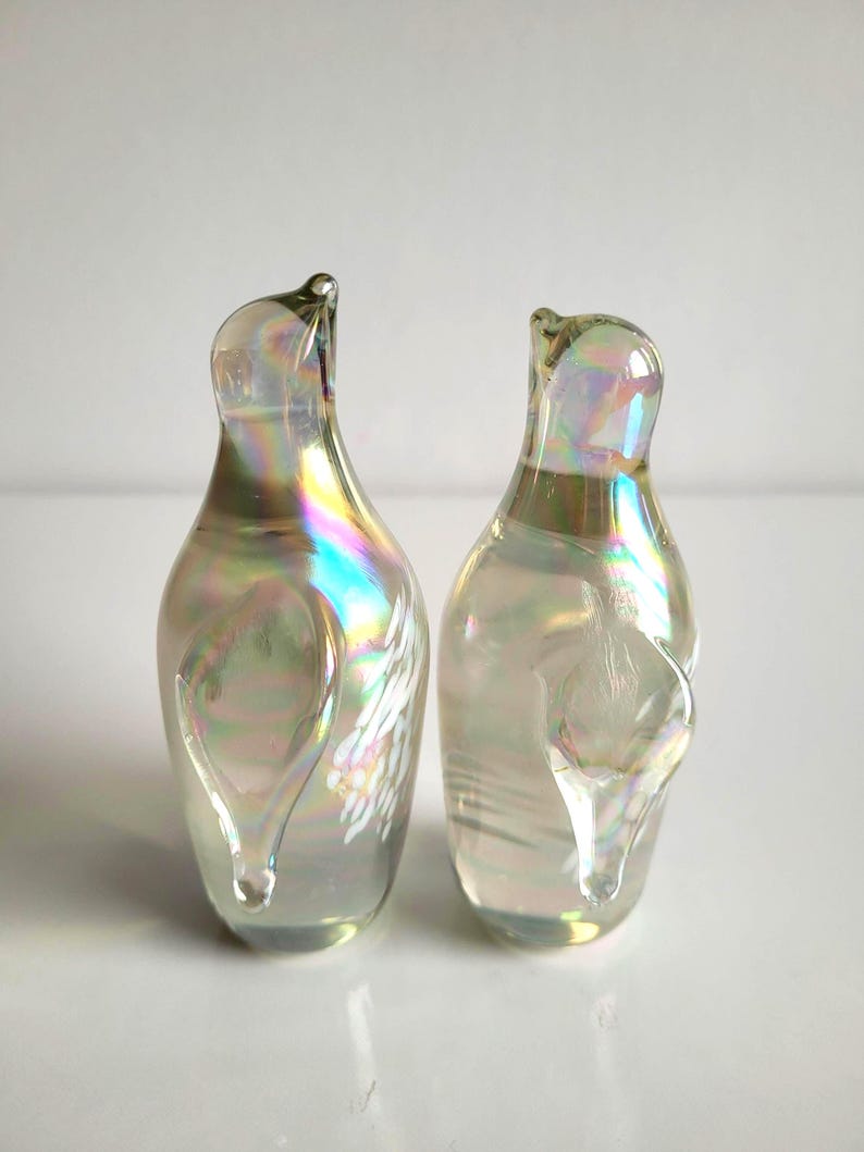 May include: Two clear glass decorative bottles with iridescent rainbow coloring. The bottles have a unique shape with a curved top and a teardrop-shaped design on the side. The bottles are displayed on a white surface.