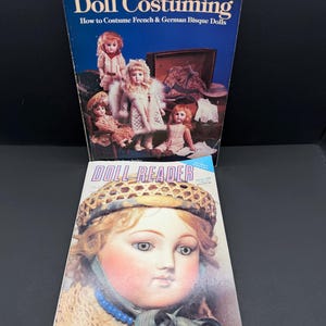 May include: Two books titled Doll Costuming: How to Costume French & German Bisque Dolls and Doll Reader. The first book features four dolls in period clothing, while the second book displays a large portrait of a doll wearing a woven hat.