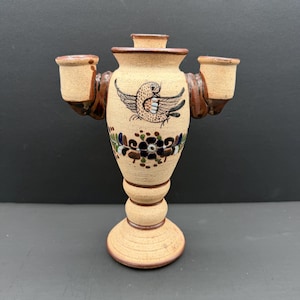 Peut inclure: Un candélabre en céramique beige à trois bougeoirs, orné d'une illustration d'oiseau brun peinte à la main et d'un motif floral bleu, vert et brun. L'objet présente une finition texturée et tachetée avec des bords brun foncé et un pied.