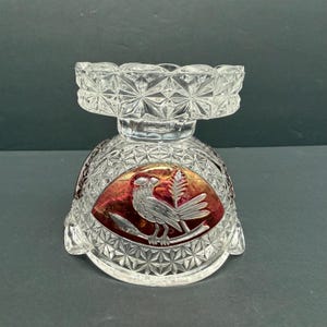 May include: Clear glass pedestal bowl with a cut crystal design. The bowl features a red and gold oval with a silver bird and wheat design. The bowl has a decorative, geometric pattern and a scalloped rim.