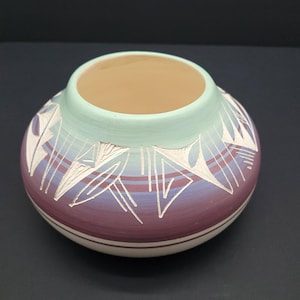May include: A handmade ceramic pot with a rounded form. The pot has a colour gradient from white at the base to a deep purple, transitioning to a light teal rim. White geometric designs are painted around the pot.