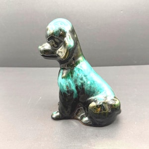 May include: A ceramic dog figurine in a sitting position, featuring a glossy finish. The dog's body is a blend of teal and black, with a shiny, reflective surface. The figurine has a classic, elegant design.