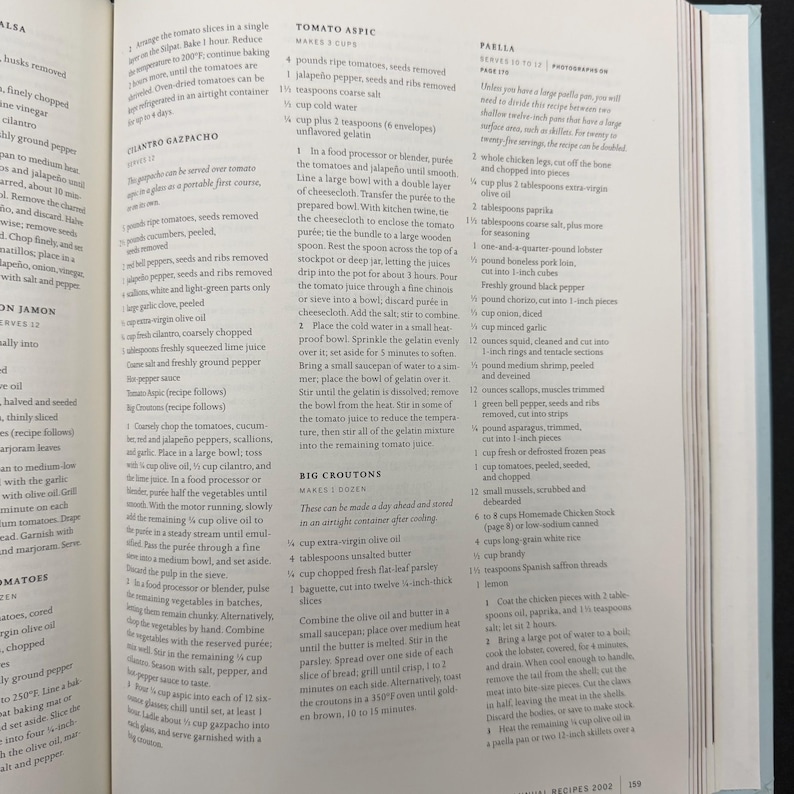 May include: Open cookbook page with recipes for Tomato Aspic, Big Croutons, and Paella. The page features text and instructions for preparing various dishes, with ingredients and measurements.