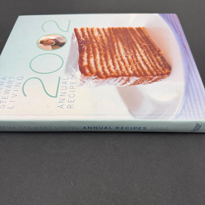 May include: A cookbook titled "Martha Stewart Living Annual Recipes 2002" with a light blue cover. The cover features a photo of a cooked dish and the number "2002" in large green numerals. The book's spine is visible.
