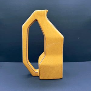 May include: A yellow ceramic pitcher with a unique, geometric design. The pitcher has a handle and a spout, and the exterior features a crackle glaze. The pitcher is approximately 25 cm tall.
