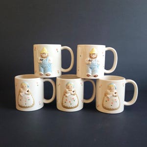 May include: Six cream-coloured ceramic mugs. Three mugs feature a relief of a man in overalls and a yellow hat, holding a tool. The other three mugs have a relief of a woman in a bonnet and apron. Each mug has small floral accents.