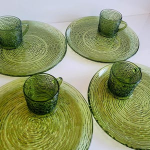 Puede incluir: Cuatro juegos de taza y platillo de vidrio verde. Cada juego incluye un plato circular texturizado y una taza a juego con asa. El vidrio tiene un patrón texturizado y acanalado. Los juegos están dispuestos sobre una superficie blanca.