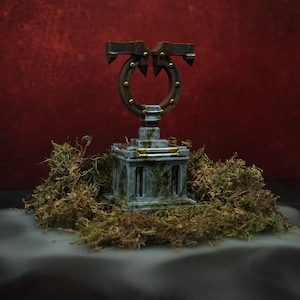 May include: A miniature stone-colored pedestal with a weathered texture and mossy accents, topped with a dark brown circular frame featuring metallic gold studs and sharp, pointed protrusions extending from the top and sides of the structure.