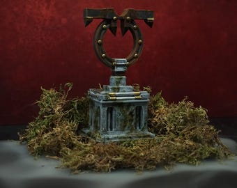 以下が含まれることがあります： 風化した質感と苔のアクセントがある石色のミニチュア台座。上部には金属製の金色の鋲が施されたダークブラウンの円形フレームがあり、構造の上部と側面からは鋭く尖った突起が伸びているデザインとなっている。