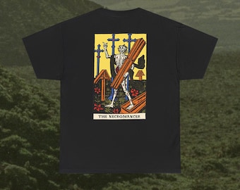 以下が含まれることがあります： 木製の棺を運ぶ骸骨のグラフィックプリントが施された黒いTシャツ。イラストには青い十字架、赤い花、黄色い背景が含まれています。長方形のデザインの下部には、黒い文字で「THE NECROMANCER」と印刷されています。