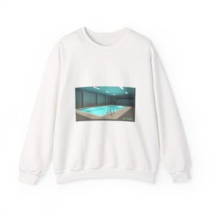May include: White sweatshirt featuring a graphic of an indoor swimming pool with turquoise water. The pool has a metal ladder and is surrounded by a concrete deck. The image is centered on the front of the sweatshirt.
