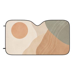 May include: Car sun shade with an abstract design. The shade features a beige background with a peach-colored sun and earth-toned shapes. A black border frames the design, and it has two small tabs for attachment.