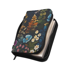 May include: A zipped notebook cover featuring a dark navy blue background with a vibrant botanical print of orange, blue, white, and pink flowers and green foliage. The cover is partially open, revealing white paper pages inside the black zipped case.