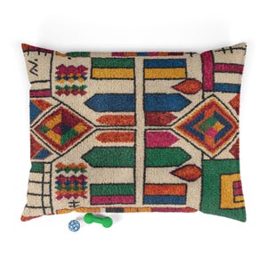 May include: A rectangular pet bed with a colorful geometric pattern in shades of beige, blue, green, orange, pink, and yellow. The bed has a textured appearance and is accompanied by a blue ball and a green dumbbell-shaped toy.