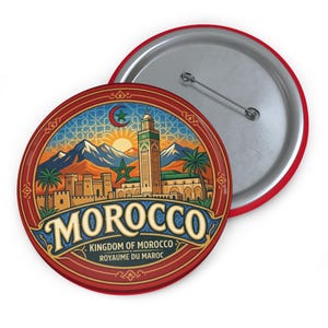Puede incluir: Un botón redondo con borde rojo y dorso plateado. El frente presenta una ilustración detallada de un paisaje urbano marroquí con la palabra "MOROCCO" en una fuente decorativa. También se incluye el texto "KINGDOM OF MOROCCO ROYAUME DU MAROC".