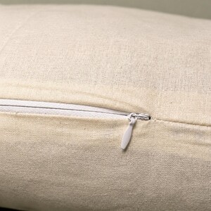 May include: Close-up of a beige linen cushion cover with a white zip. The zip is partially open, revealing the interior. The fabric has a textured appearance.