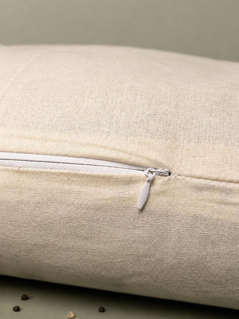 May include: Close-up of a beige linen cushion cover with a white zip. The zip is partially open, revealing the interior. The fabric has a textured appearance.