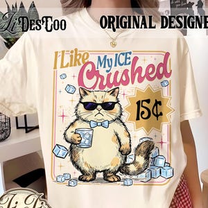 Op de afbeelding: Crèmekleurig T-shirt met een cartoonkat met een zonnebril en een vlinderdas, die een glas ijs vasthoudt. De tekst "I Like My ICE Crushed" en "15¢" worden weergegeven. Het shirt heeft de tekst "ORIGINAL DESIGNER" bovenaan.