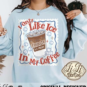 May include: Light blue sweatshirt with a coffee-themed graphic. The design features a coffee cup filled with ice cubes and the text "Only Like Ice In My Coffee". The graphic is framed with a postage stamp design.