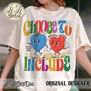 May include: Cream-colored t-shirt with a colorful graphic design. The design features the words "CHOOSE TO INCLUDE" in rainbow colors, along with two cartoon hearts holding hands. The text "INCLUSION MATTERS" and "BE KIND TO ALL KINDS" are also included.