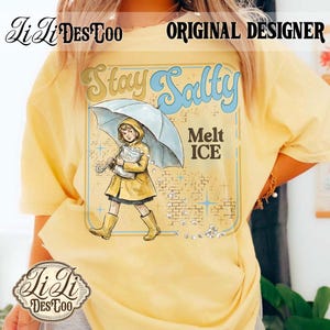 Pode incluir: Camiseta amarela clara com um desenho de uma crian&ccedil;a de capa e botas amarelas, segurando um guarda-chuva e um saco de gelo. O texto na camiseta diz "Stay Salty" e "Melt ICE". O design &eacute; de estilo retr&ocirc;.