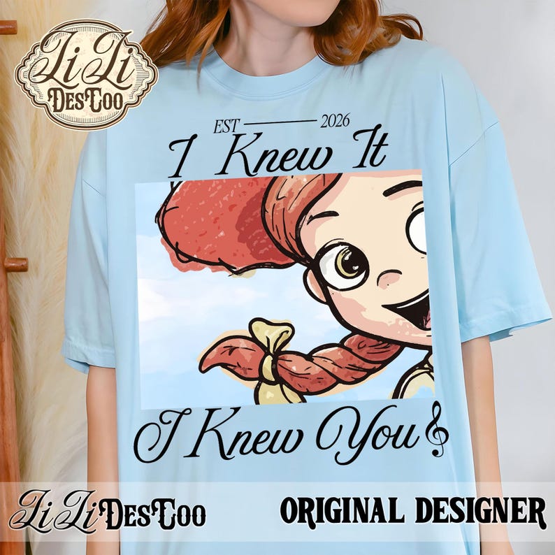 K&ouml;nnte beinhalten: Ein hellblaues T-Shirt mit einem Grafikdruck einer Zeichentrickfigur mit roten Z&ouml;pfen. Der Text &uuml;ber der Grafik lautet "EST 2026 I Knew It" und der Text darunter "I Knew You". In der oberen linken Ecke befindet sich ein Logo mit "Li Li DES TOO".
