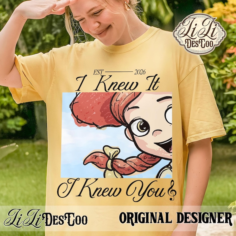 K&ouml;nnte beinhalten: Ein gelbes T-Shirt mit kurzen &Auml;rmeln und einer Grafik einer Zeichentrickfigur mit roten Haaren und einem Zopf. Der Text lautet EST 2026, I Knew It und I Knew You. Das Design enth&auml;lt ein Logo in der oberen rechten Ecke mit Li Li DES TOO.
