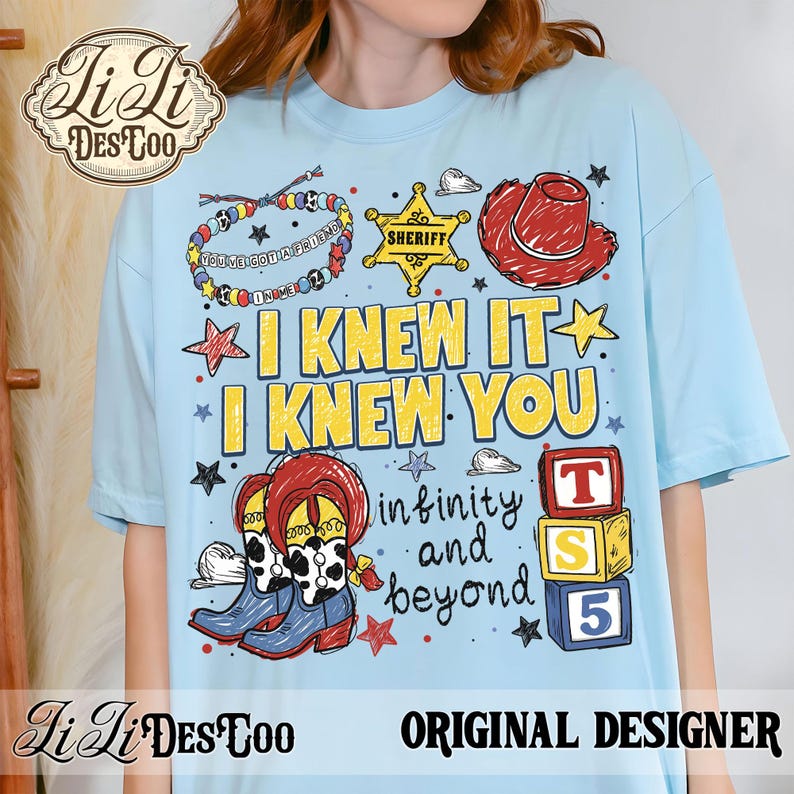 Op de afbeelding: Een lichtblauw t-shirt met een grafische print van een kralenarmband, een gele sheriffster, een rode cowboyhoed en laarzen met koeienvlekken. De tekst luidt I KNEW IT I KNEW YOU, infinity and beyond, en TS 5 op gestapelde blokken.