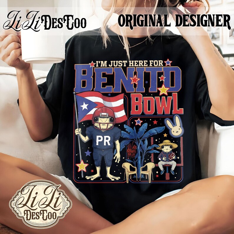 May include: Black t-shirt with a graphic featuring a frog in a football uniform holding a Puerto Rican flag. Text reads "I'M JUST HERE FOR BENITO BOWL" with a bunny and other tropical elements. The shirt has the designer's logo.
