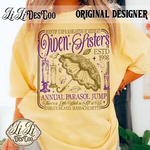 May include: A pale yellow t-shirt featuring a graphic print with purple and brown ink. The design includes an ornate parasol, three lit candles, and text reading "Owen Sisters ESTD 1998", "Annual Parasol Jump", and "There's a Little Witch in All of Us".