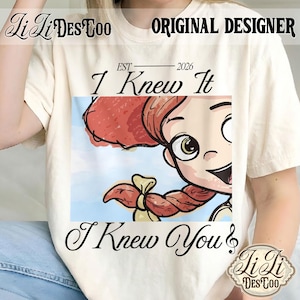 K&ouml;nnte beinhalten: Ein cremefarbenes T-Shirt mit einem Grafikdruck einer Zeichentrickfigur mit roten Z&ouml;pfen. Der Text lautet "EST 2026", "I Knew It" und "I Knew You" mit einem Violinschl&uuml;ssel. Das T-Shirt zeigt zudem "Li Li DES TOO" und "ORIGINAL DESIGNER".