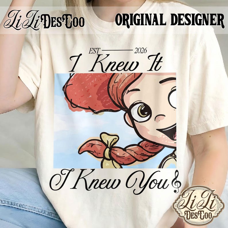 K&ouml;nnte beinhalten: Ein cremefarbenes T-Shirt mit einem Grafikdruck einer Zeichentrickfigur mit roten Z&ouml;pfen. Der Text lautet "EST 2026", "I Knew It" und "I Knew You" mit einem Violinschl&uuml;ssel. Das T-Shirt zeigt zudem "Li Li DES TOO" und "ORIGINAL DESIGNER".
