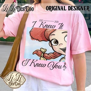 K&ouml;nnte beinhalten: Ein hellrosa T-Shirt mit kurzen &Auml;rmeln und einem Grafikdruck einer Zeichentrickfigur mit roten Haaren und einem Zopf. Der Text "EST 2026 I Knew It" steht &uuml;ber der Grafik und "I Knew You" ist in einer schwarzen Schreibschrift darunter gedruckt.